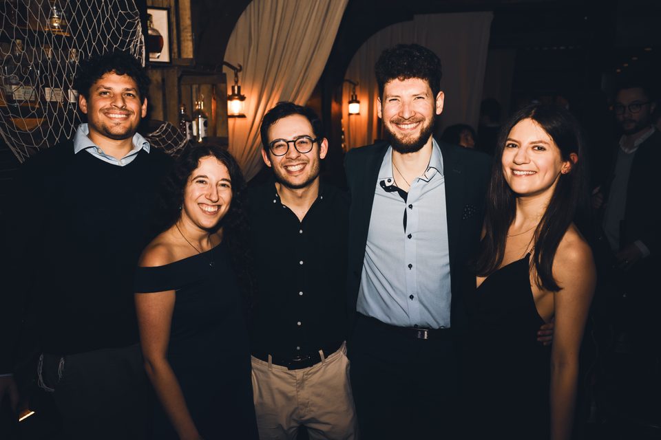 Five people posing together in a dimly lit indoor venue.