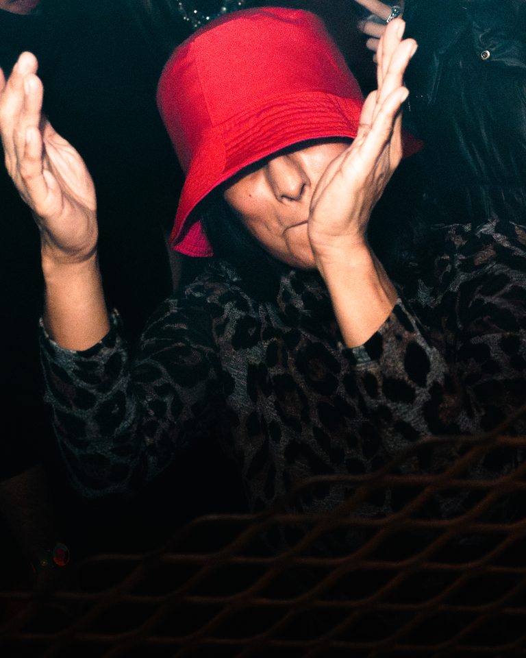 Person in red hat clapping, dark background, indoor setting.