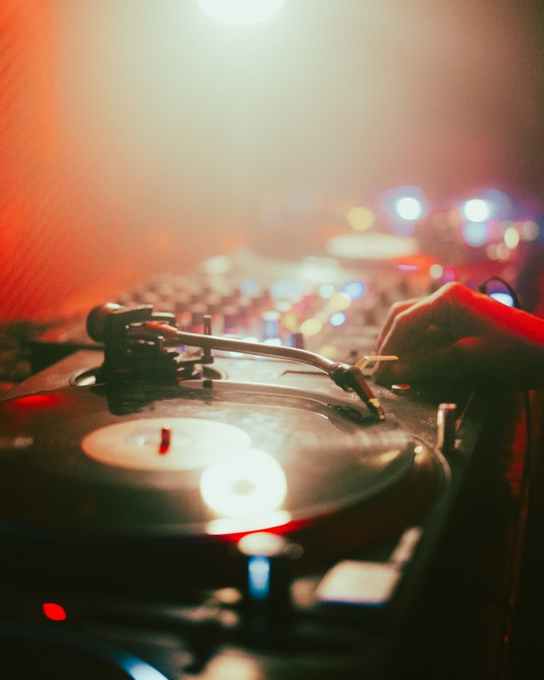 Hand adjusting vinyl on turntable under stage lights in a dim club.