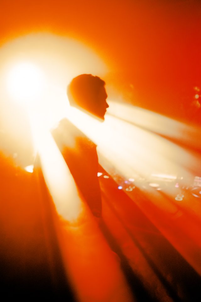 A performer's silhouette against bright orange stage lights, captured in medium shot.